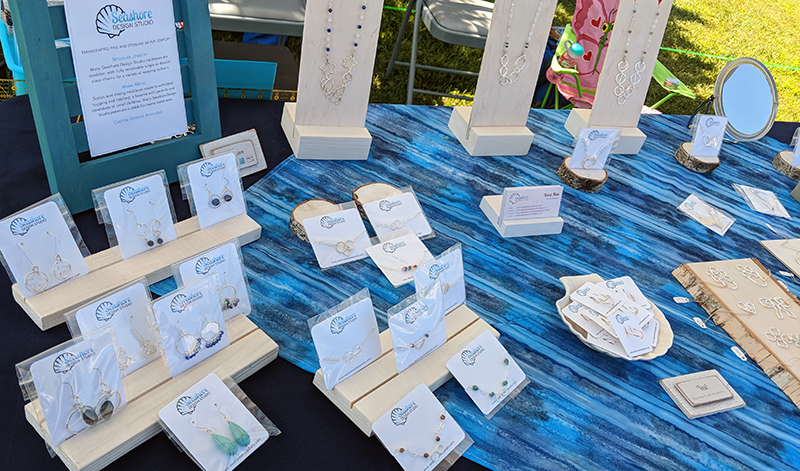 Seashore Design Studio craft fair table dressed in shades of blue and white, with jewelry in displays